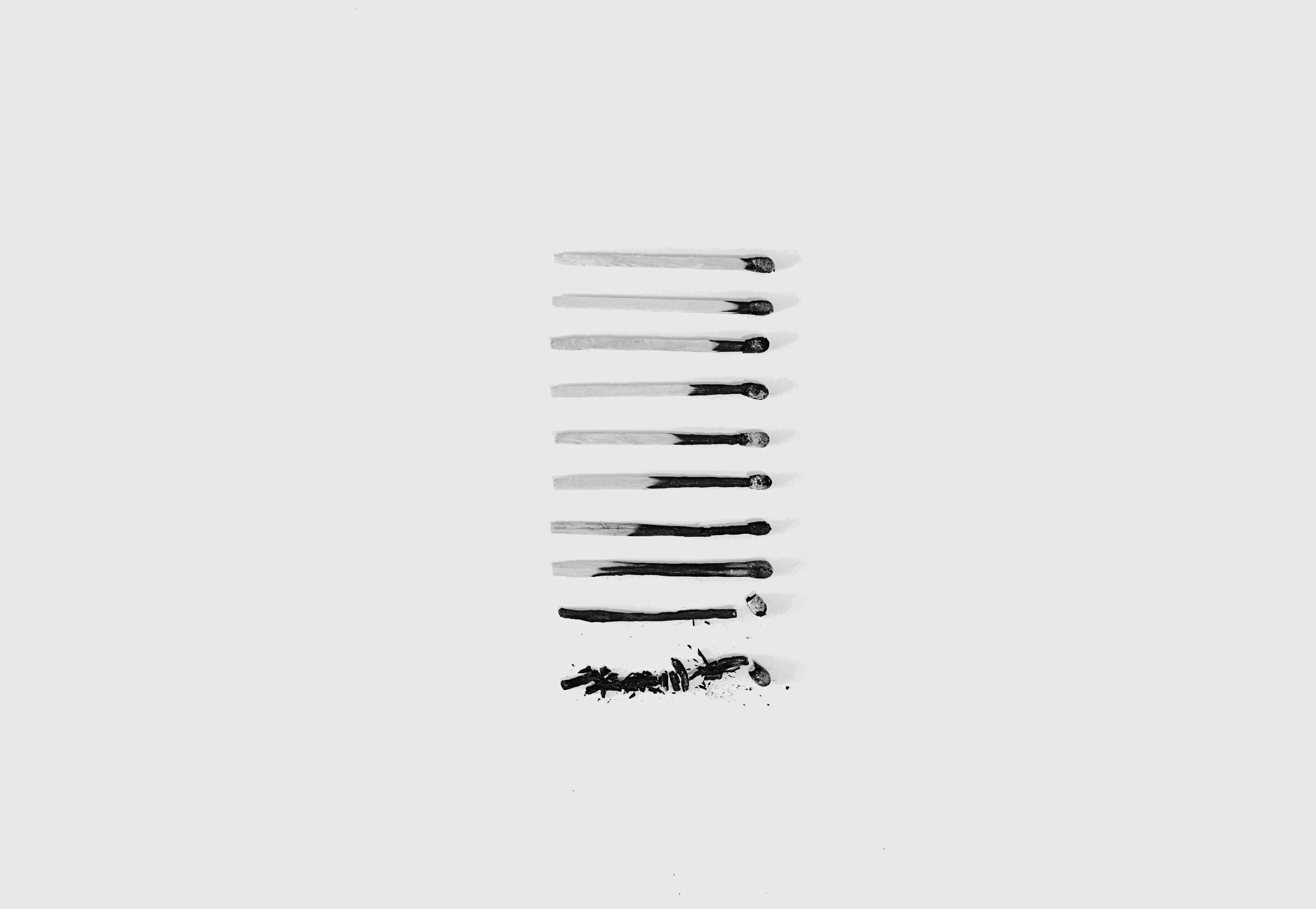 Ten matches arranged vertically, showing progressive stages of burning from top to bottom. The first match is nearly pristine with only a slightly charred tip, and each subsequent match shows increasing burn damage, until the last two, where one is burned to a fragile black sliver and the final match has completely disintegrated into ash.